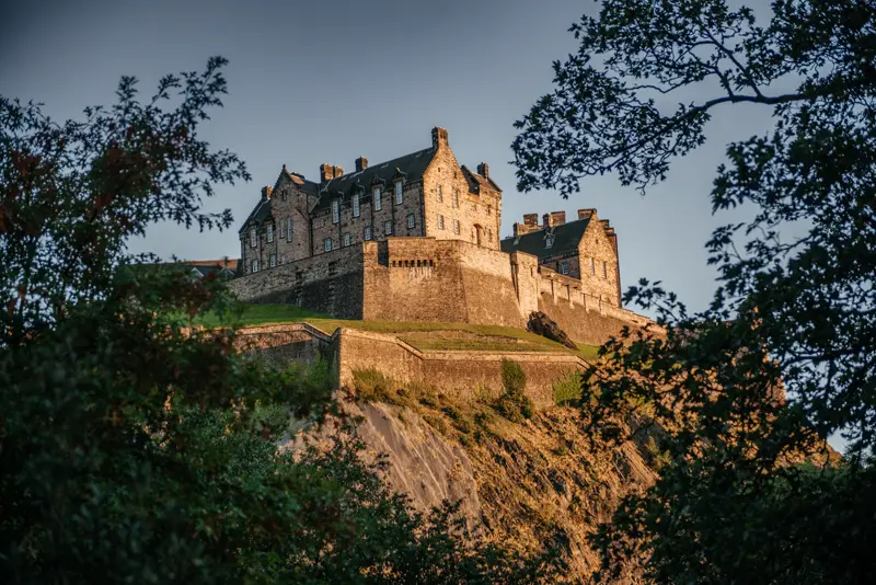 Edinburgh Castle glowing on its rock at golden hour, framed by trees