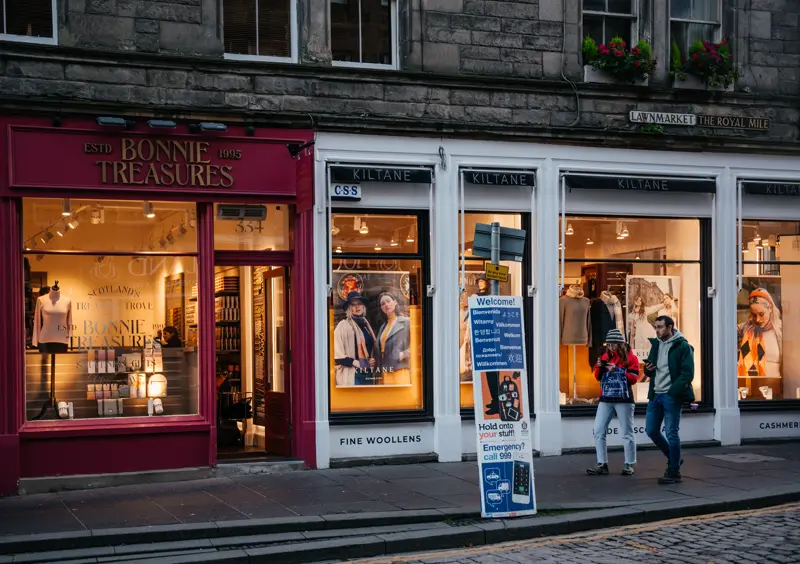 Lit shopfronts on the Lawnmarket of the Royal Mile at dusk